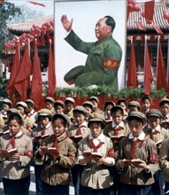 Children reading from mao's little red book at a rally with a portrait of mao in the background.