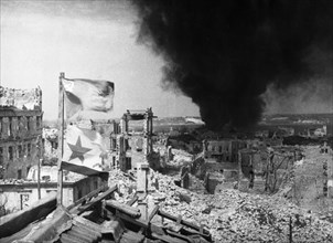 World war 2, siege of sevastopol, soviet flags on the roof of a building occupied by soviet troops in the port of sevastopol, a german tanker is burning in the bay in the background, 1942.