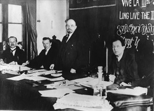 V,i, lenin (standing) presides at first congress of comintern (third international) in kremlin, march 1919, moscow, soviet union, left to right: klinger, eberlaine (?), lenin, f, patten (?), legend on...