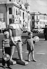 A robot belonging to local circus performer oleg sokol helping two children with balloons cross the street in arkhangelsk, ussr, 1967, the robot is part of the technical illusion attraction 'wonders w...