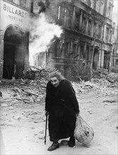 An old german woman walks through the smoking ruins of berlin after the city was captured by the red army, world war 2, german defeat, 1945.