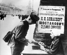The billboard of the performing of the seventh symphony by d, shostakovich, a soviet soldier buying a ticket to the concert in leningrad, 1942.