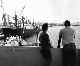 A man and a woman looking over a new fishing port built in the harbor of havana with technical assistance provided by the soviet union, july 1969, a soviet fishing vessel is on the left.