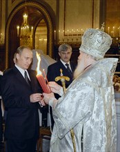 Patriarch of moscow and all russia alexy ll handing to president of russia vladimir putin a candle lit of the holy fire brought from jerusalem, at the easter service at the christ the saviour cathedra...