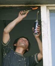 A north korean guest worker repairs a window, in vladivostok, russia, january 28 2003,russian businessmen like to hire foreign citizens (chinese, vietnamese, north koreans) who agree to work under any...