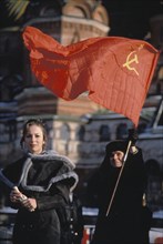 A young woman with a man carrying a soviet hammer and sickle flag during an anti-government demonstration in red square, early 1990s.