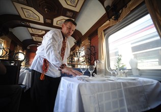 Moscow, russia, august 16, 2011, waiter in traditional russian costume lays the table in a diner car on a moscow-to-beijing passenger train