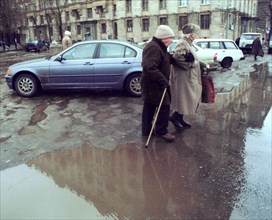 Moscow, russia, february 5, 2002, an old couple trying to cross a street on tuesday, after the recent thaw, with day temperatures reaching up to 4 degrees celsius, roads are covered with puddles of me...