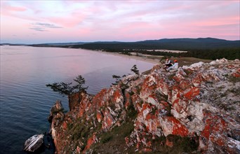Irkutsk region, russia, september 5, 2006, tourists sit on cliffs on olkhon island, a view of red cliffs on olkhon island and baikal’s saraisky bay.