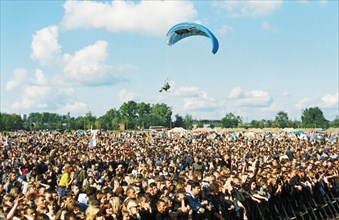 A powered paraglider flying over a crowd of fans at the 'invasion' outdoor rock festival at ramenskoye, moscow, russia, 2000.