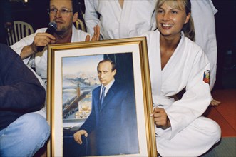 Television announcer (tv6) olesya loseva holding a portrait of vladimir putin at a judo tournament commemorating the 1rst anniversary of putin's presidency, march 2001.
