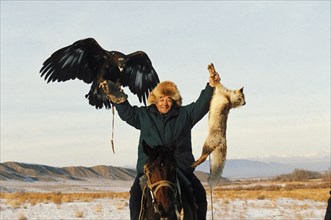 Kazakh hunter, toregendy chormanov, with his golden eagle, holding a fox they had cought, kazakhstan, november 1999.