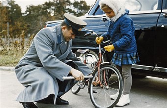 Cosmonaut yuri gagarin helping his daughter, lena, to put air in the tire of her bicycle.