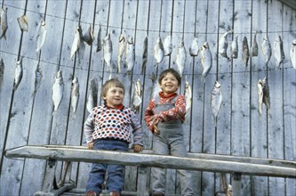 Two boys in front of a house with drying fish in th irkutsk region of siberia, 1990s.