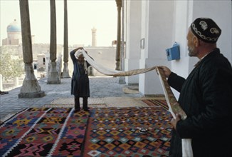 A man helping another to put on a 19 meter long turban in bukhara, uzbekistan, 1990s.
