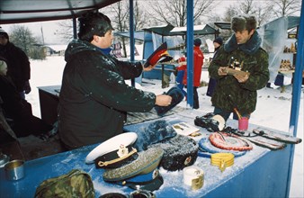 A man selling soviet military hats at the outdoor market (vernissazh) in izmailovo park, moscow, russia where all sorts of things are sold including soviet souvenirs and various arts and crafts, 1990s...