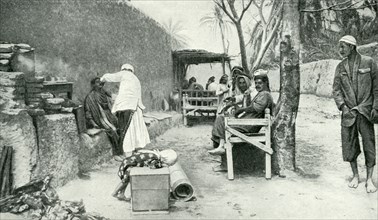 Historical Geography. 1900. Iraq. Patient customers waiting their turn in the open-air establishment of a wayside barber of Iraq.