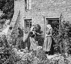 Historical image of two women standing outside a stone house talking at the doorway