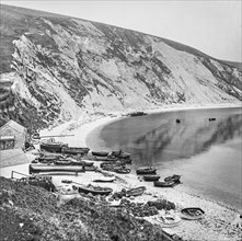 Fishing village on Lulworth Cove with boats on the shore and cliffs along the coast
