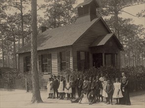 African American school children posed with their teacher outside a school, possibly in South Carolina