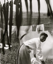 Black and white, an informal portrait of a young Negro woman surrounded by laundry in Newport, R.I.