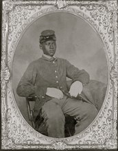 Seated black soldier, frock coat, gloves, kepi