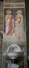 Italy. Florence. Mural painting with saints and stoup. 14th-15th century. Basilica of San Miniato al Monte.