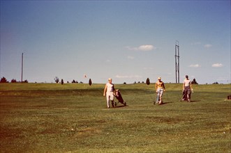 Men on the fairway of a golf course carrying their golf bags circa 1957-1960.