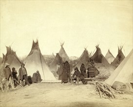 Group of twelve Miniconjou (children and adults)--many are looking away from camera--in a tepee camp, probably on or near Pine Ridge Reservation. 1891.