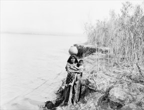 Edward S. Curits Native American Indians - Mohave Indian woman carrying water on her head and holding child circa 1903.