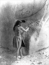 Edward S. Curtis Native American Indians - Paviotso man standing, marking side of glacial boulder that already has petroglyphs on it ca.1924.