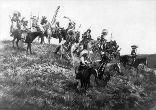 Edward S. Curits Native American Indians - Several Oglala men, many wearing war bonnets, on horseback riding down hill circa 1907.