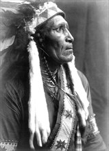 Edward S. Curtis Native American Indians - Raven Blanket, wearing several necklaces and warbonnet with ermine streamers circa 1910.
