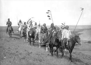 Edward S. Curtis Native American Indians - Small band of Atsina men on horseback, some carrying staffs with feathers, one wearing a war bonnet circa 1908.
