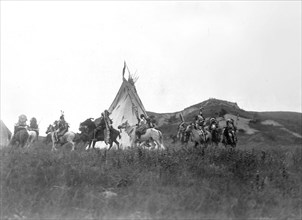 Edward S. Curits Native American Indians - Several Dakota men on horseback riding in a circle around a tipi circa 1907.