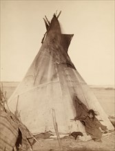 A young Oglala girl sitting in front of a tipi, with a puppy beside her, probably on or near Pine Ridge Reservation 1891.