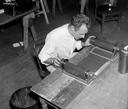 A worker is shown inspecting a roll of film for flaws before it is sent to the laboratory to be printed circa 1937.