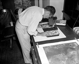 A worker is shown making a stereoscopic examination of the finished photographic prints to determine the relief or elevation of land surface for a map of the United States circa 1937.