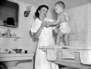 A woman in a bathoom putting powder on a baby circa 1937.