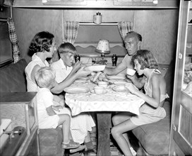 Family eating a meal inside their camper trailer circa 1937.