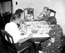 Family eating a meal together at the dinner table circa 1937.