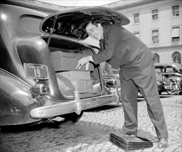 Man in suit packing the trunk of his car for a journey home circa 1938.