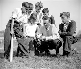 Hall of Fame pitcher Walter Johnson discussing the finer points of the game of baseball with young children circa 1940.