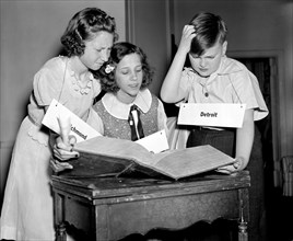 The Courier-Journal spelling bee participants in staged photo, looking up words in a dictionary, 1940.
