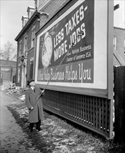 Chamber of Commerce poster being pasted on a billboard touting lower taxes circa 1939.