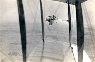 Photograph of Curtiss JN-4 aircraft C187 in flight, with a man [Lieutenant Ned Ballough] 'wing walking': standing with his arms on the top of the wing and his feet behind the back of the cockpit circa...