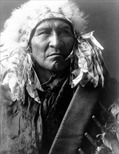 Edward S. Curits Native American Indians - Photograph shows Bread, an Apsaroke Indian, wearing a headdress circa 1908.