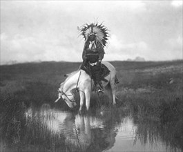 Edward S. Curtis Native American Indians - Cheyenne Indian, wearing war bonnet headdress, on horseback at a pool of water circa 1905.