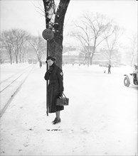 Woman standing in the snow underneath a 'car stop' sign circa 1936.