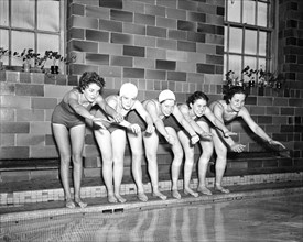 Women swimmers preparing to dive into a swimming pool circa 1936.